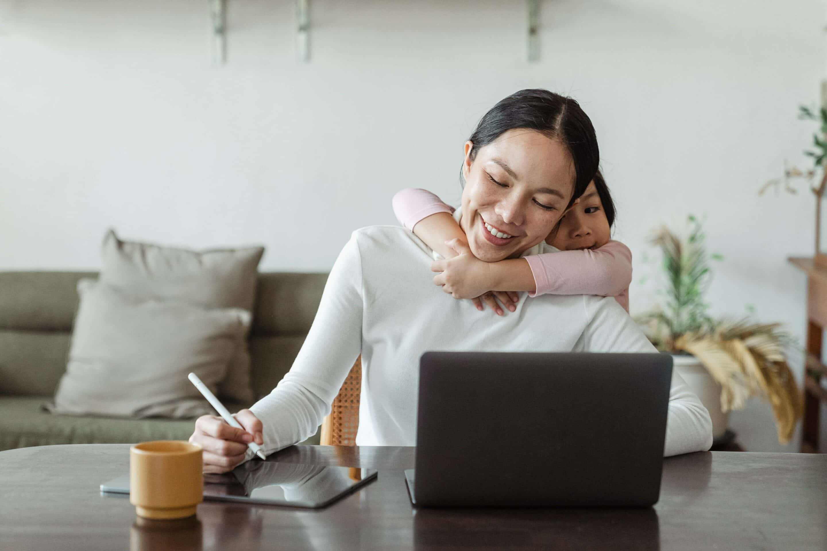 Smiling woman enjoying the benefits of flexible working while working from home with her child.
